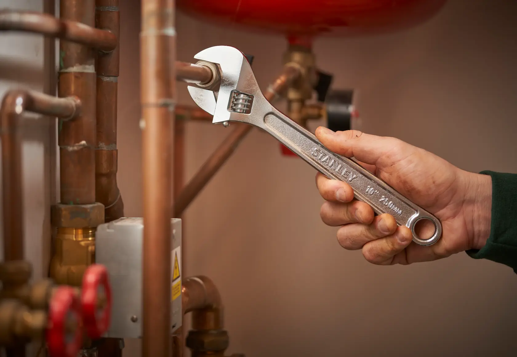 Photo of STANLEY STHT13123-0 adjustable wrench being used on copper pipes in a plumbing setting.