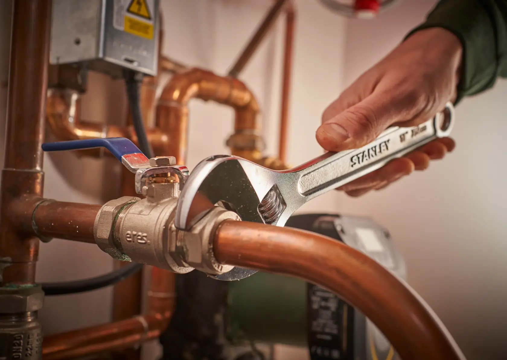 STANLEY STHT13156-0 adjustable wrench in use on copper plumbing pipes, close-up indoor photo.
