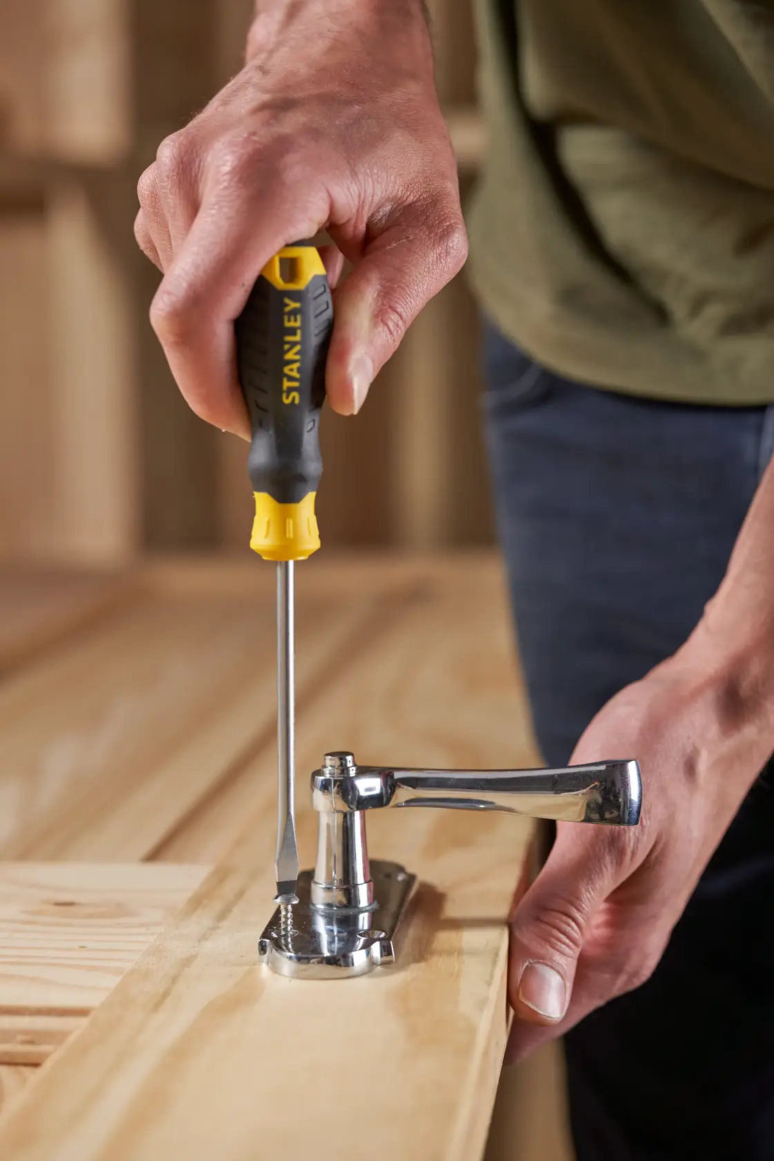 Photo of STANLEY STHT16146-0 screwdriver in use tightening a metal hinge on a wooden surface.