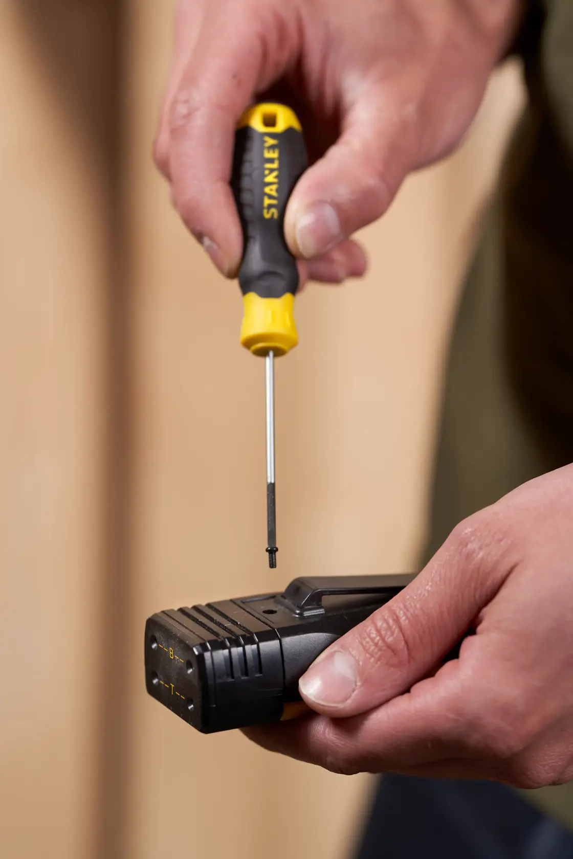 Photo of STANLEY STHT16151-0 screwdriver with yellow and black handle in use on a black electronic device held by hand.
