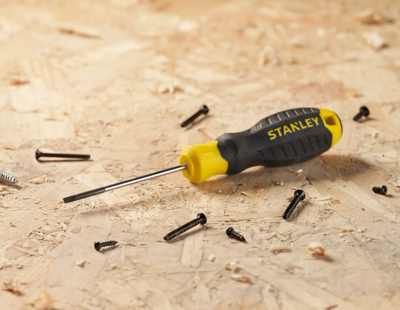 STANLEY STHT16151-0 flathead screwdriver with yellow and black handle on wood surface, surrounded by screws.