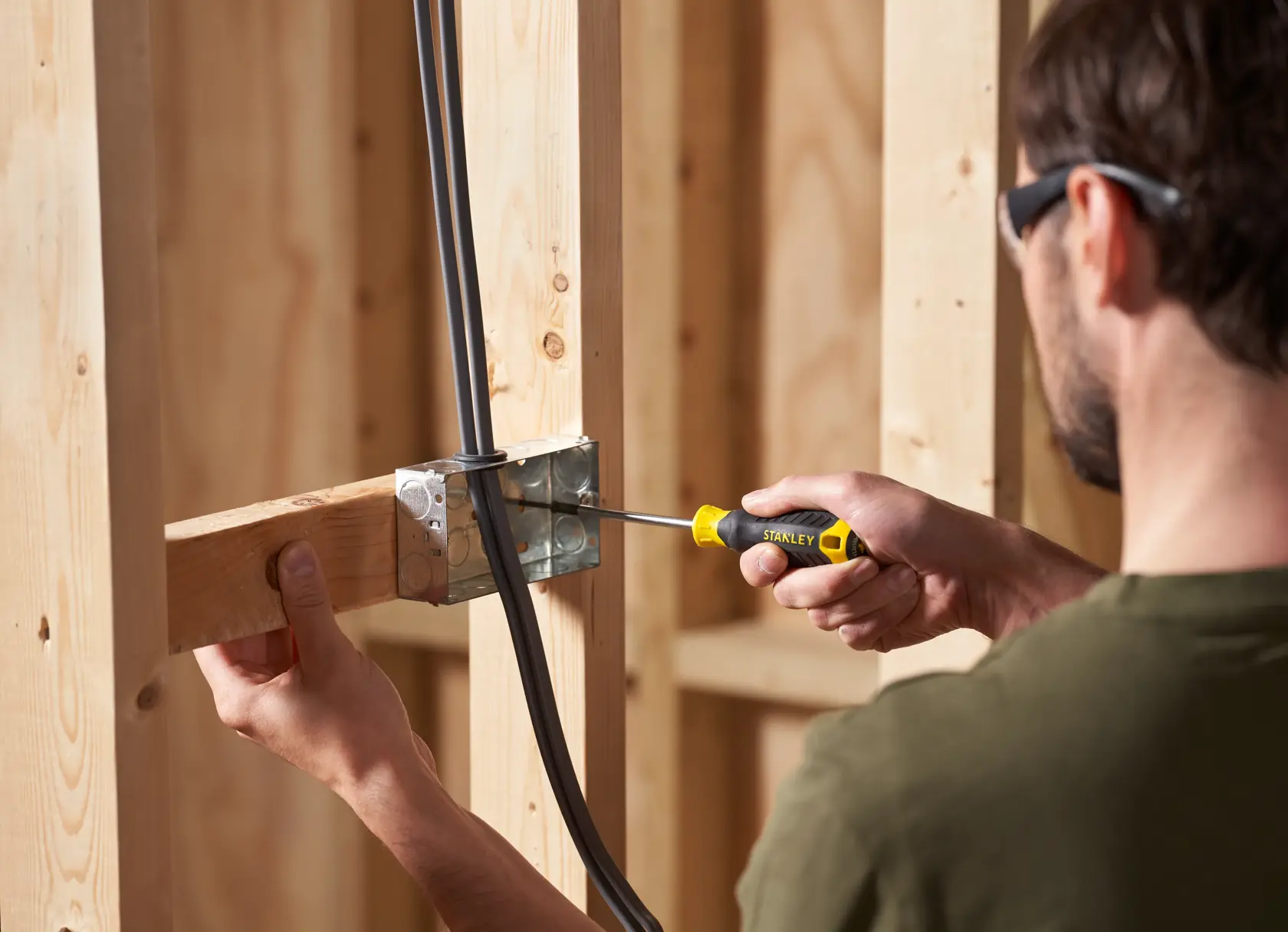 STANLEY STHT16163-0 screwdriver in use tightening a screw in a metal electrical box with wooden studs, close-up.