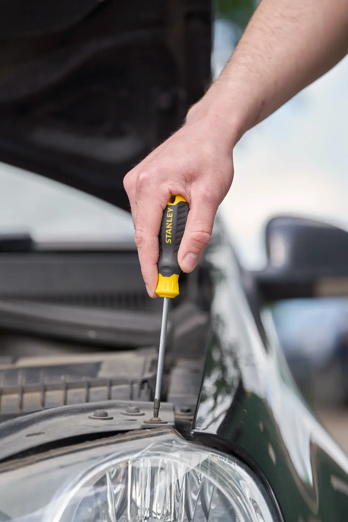 STANLEY STHT16179-0 screwdriver used on a car engine, black and yellow ergonomic handle.
