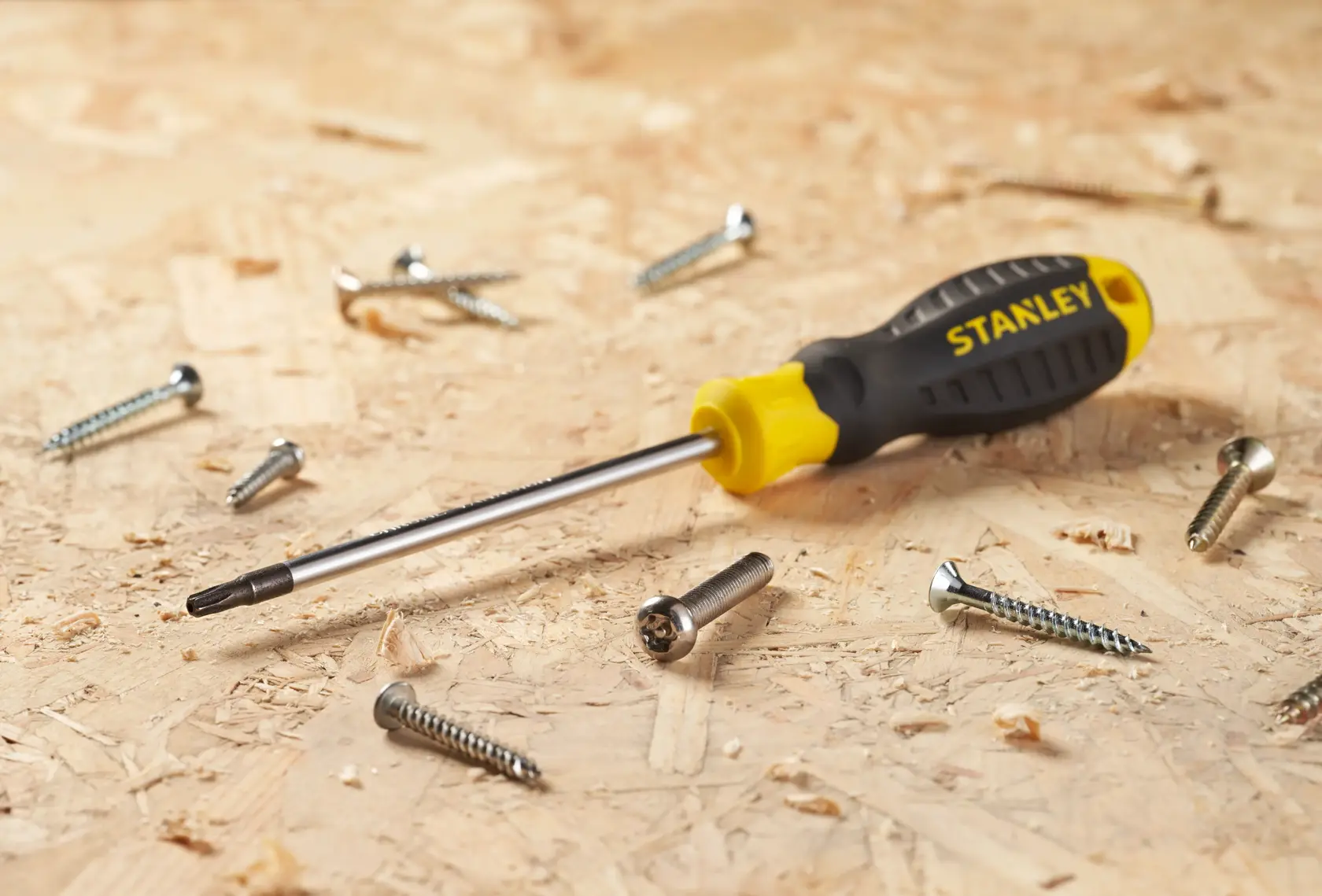STANLEY STHT16179-0 screwdriver with black and yellow handle on wood surface, surrounded by metal screws, side angle.