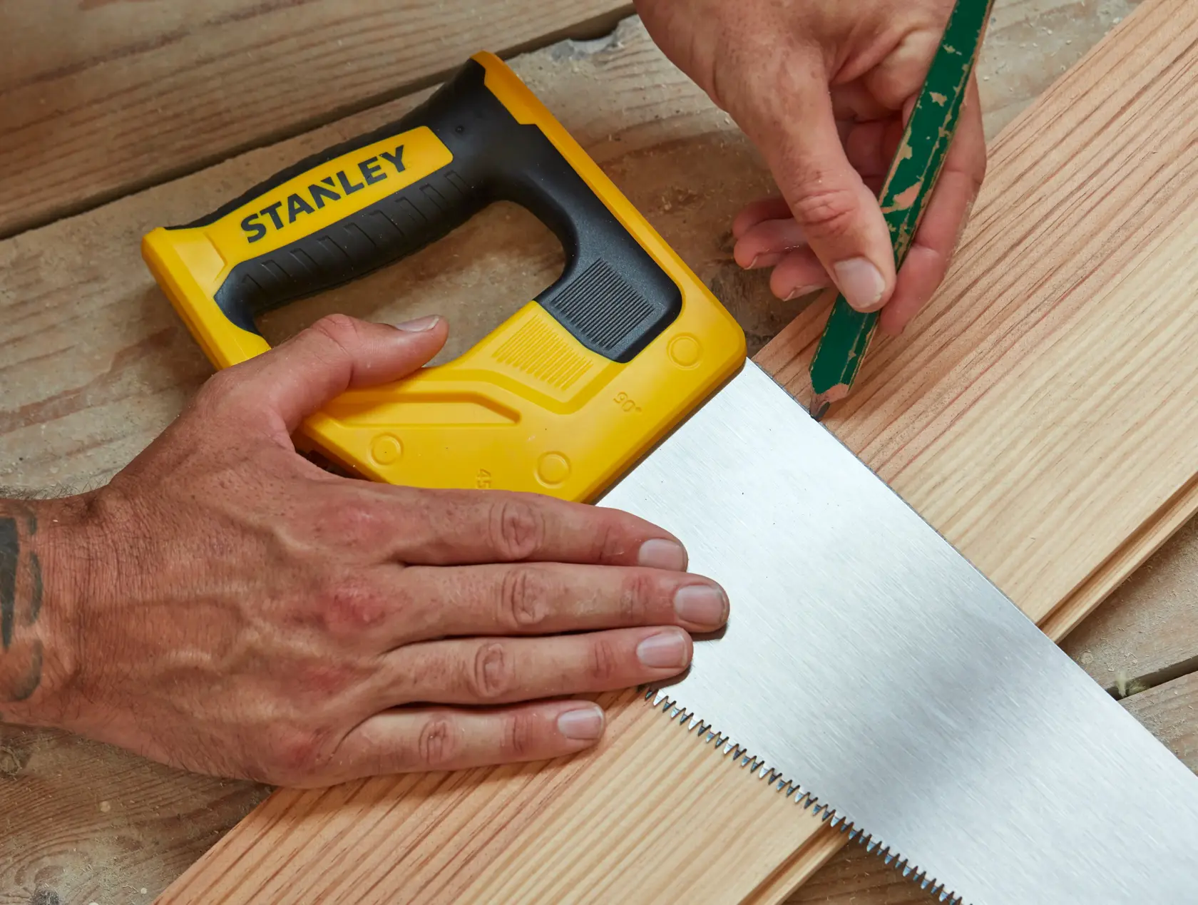 Stanley STHT20350-1 scie à main avec poignée jaune et noire sur bois, personne marquant au crayon.