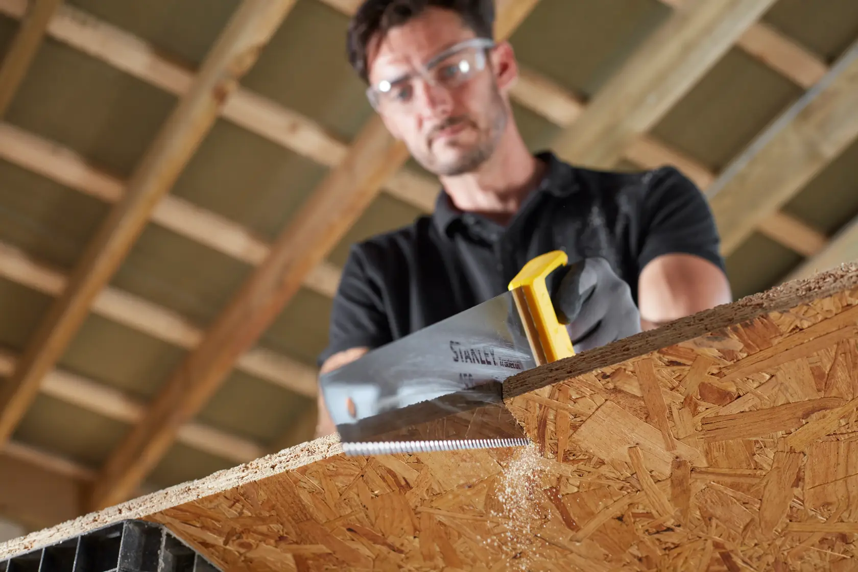 STANLEY STHT20354-1 scie à main avec poignée jaune coupant un panneau en bois dans un atelier de menuiserie.