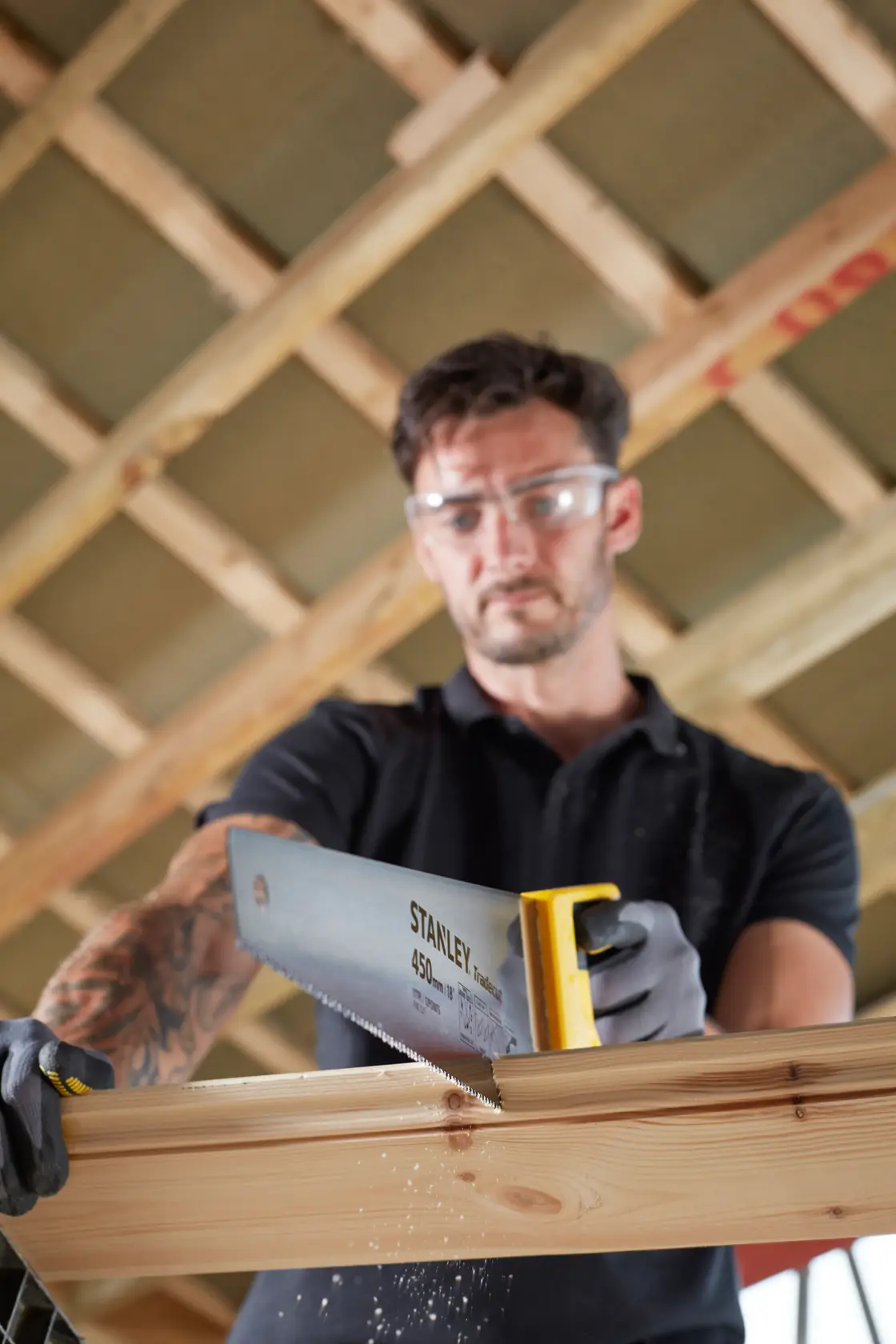 Photographie de la scie à main STANLEY STHT20355-1 avec poignée jaune, coupant une poutre en bois à l'intérieur.