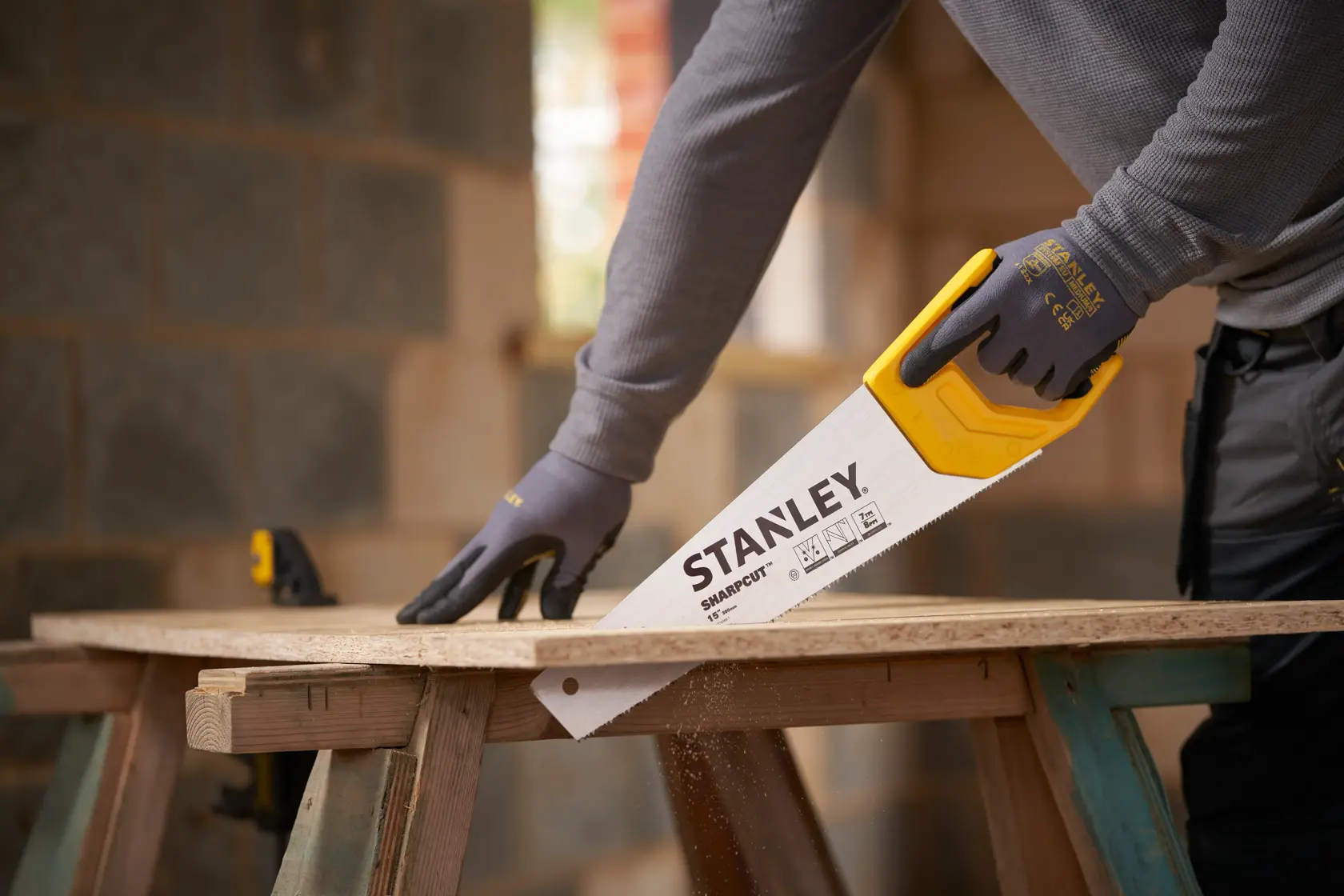 Photographie de la scie à main STANLEY STHT20366-1 avec poignée jaune coupant du bois, utilisée par une personne gantée.