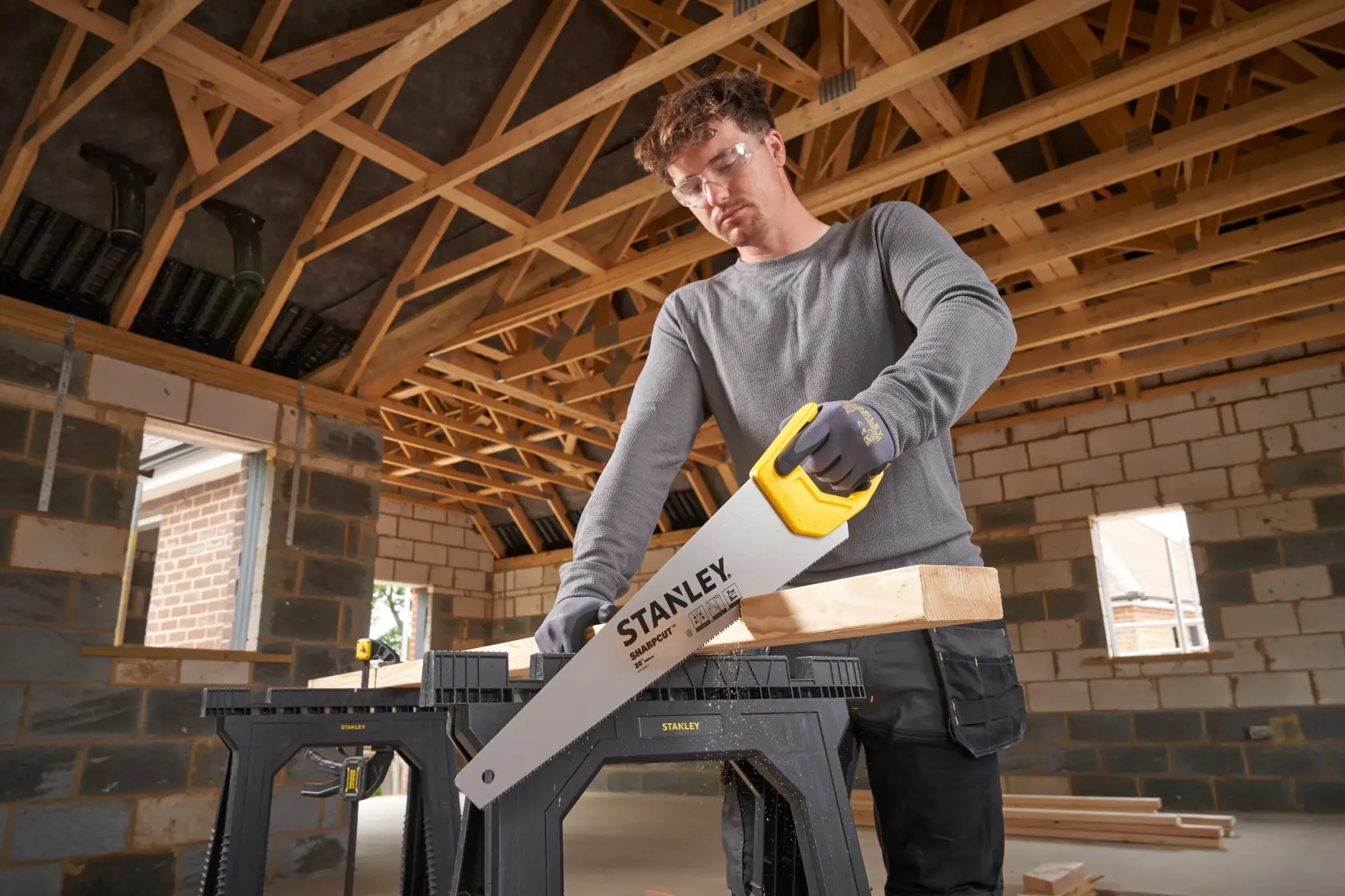 Photo of STANLEY STHT20367-1 hand saw with yellow handle, cutting wood on a sawhorse in a building under construction.