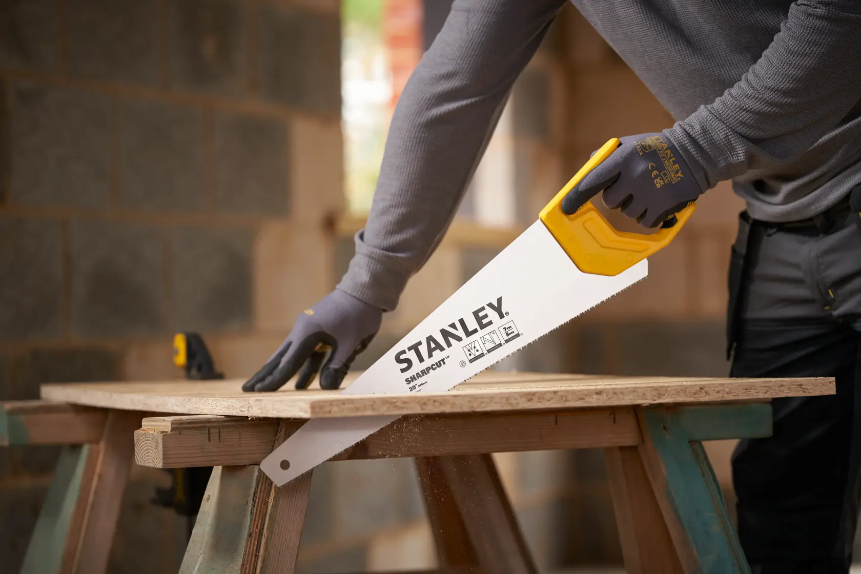 STANLEY STHT20367-1 hand saw with yellow handle cutting wood, side angle view, used by person wearing gloves.