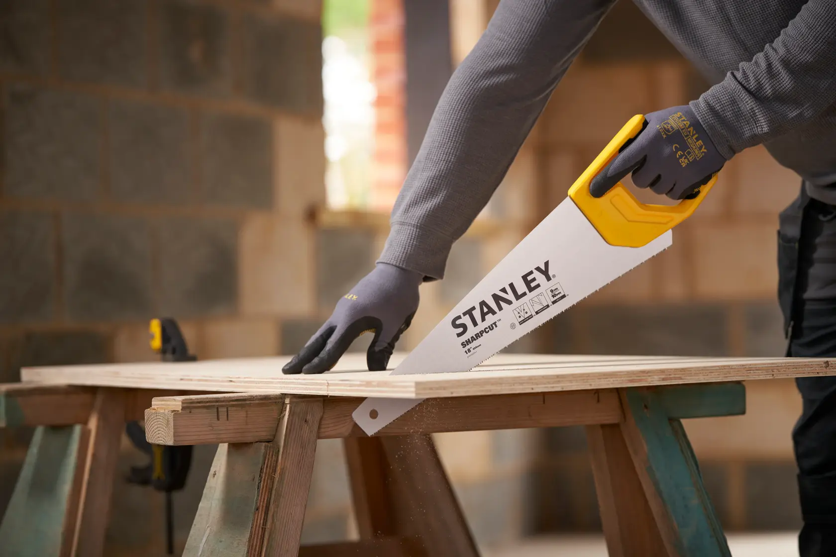 STANLEY STHT20374-1 hand saw with yellow handle cutting wood, shown in use by a person wearing gloves.