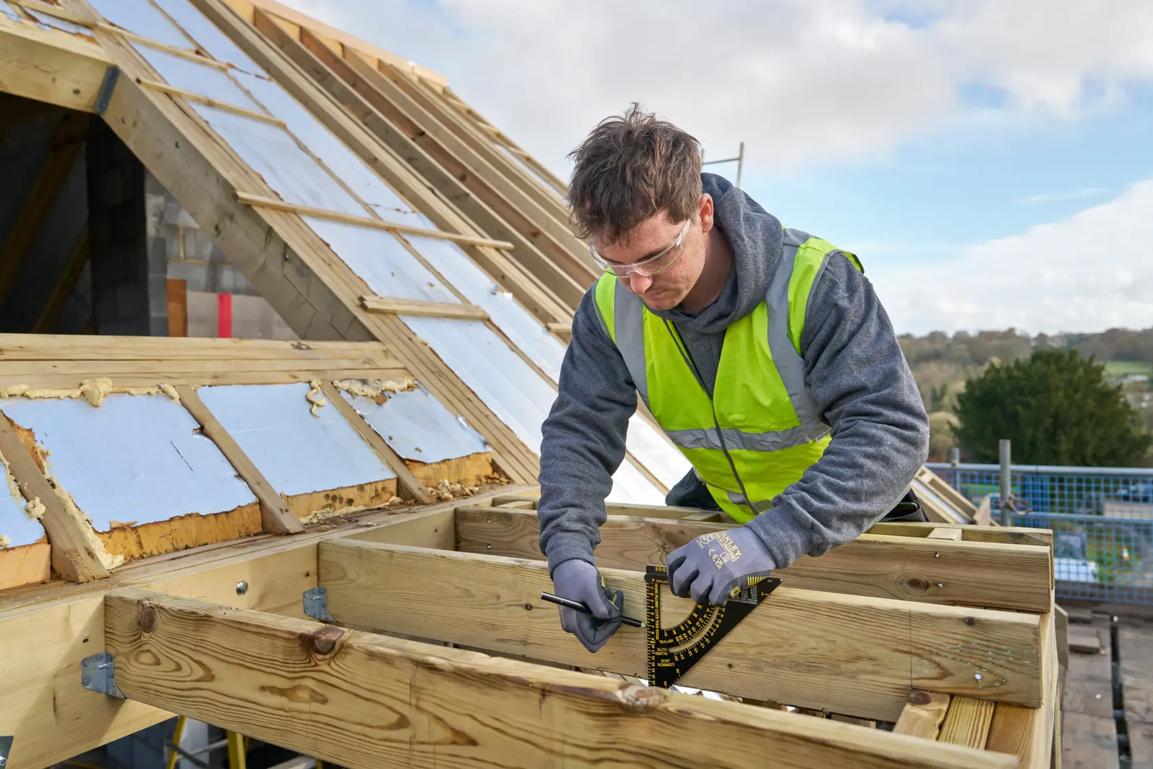 STANLEY STHT46056-0 roofing square held by worker measuring timber frame on construction site.