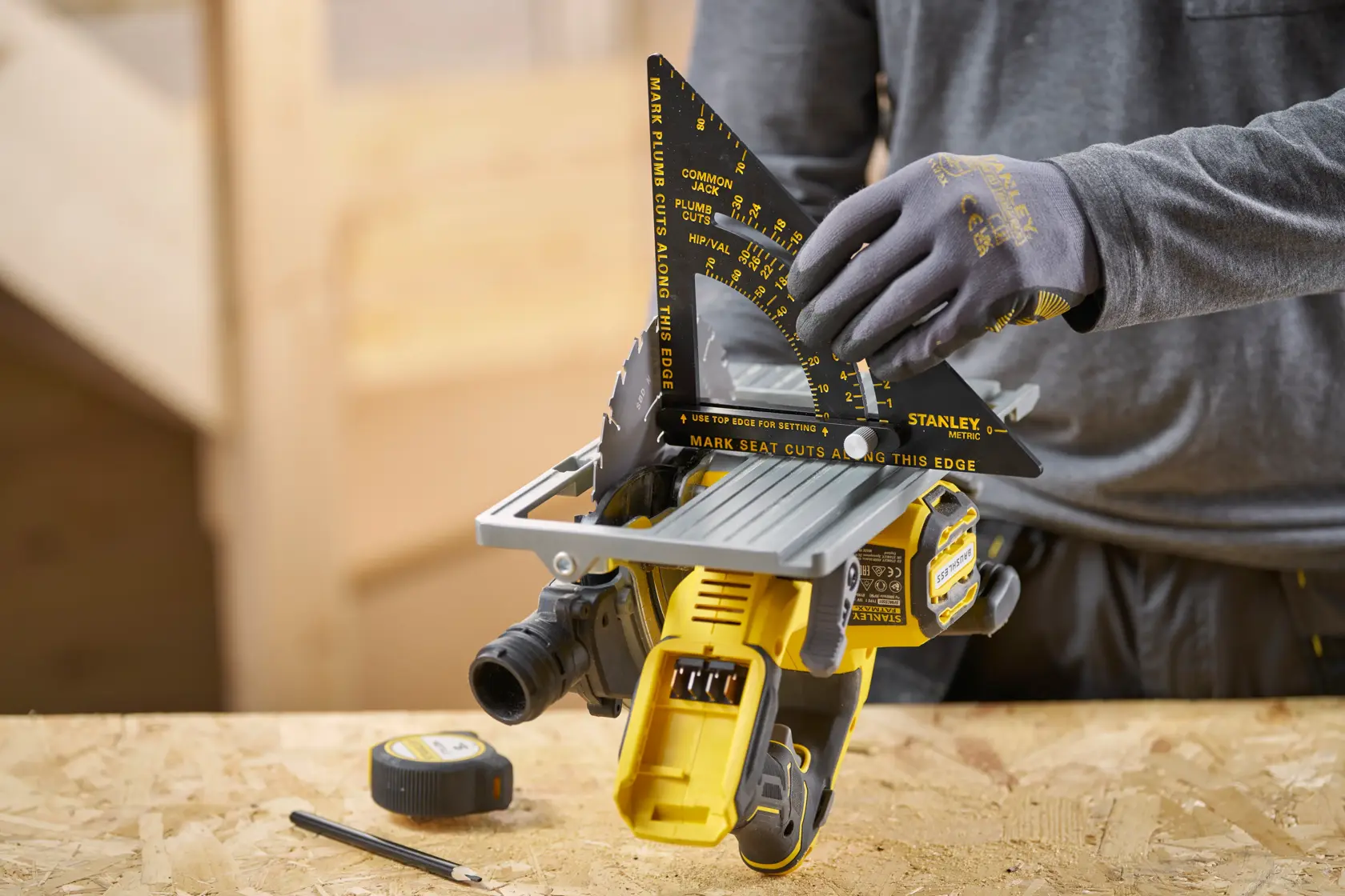 STANLEY STHT46056-0 rafter square in use, measuring saw angle, on a woodworking table with tape measure and pencil.