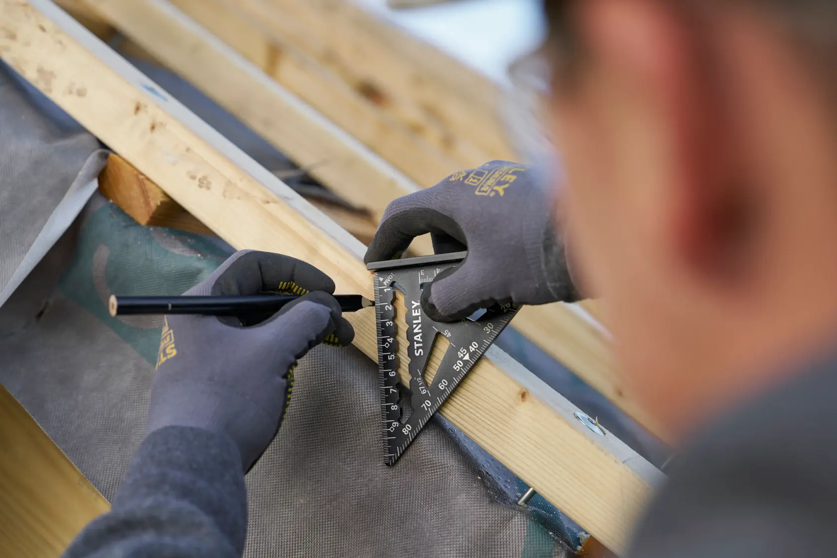Foto della squadra da carpentiere STANLEY STHT46100-0 usata per segnare il legno, primo piano su mani con guanti.