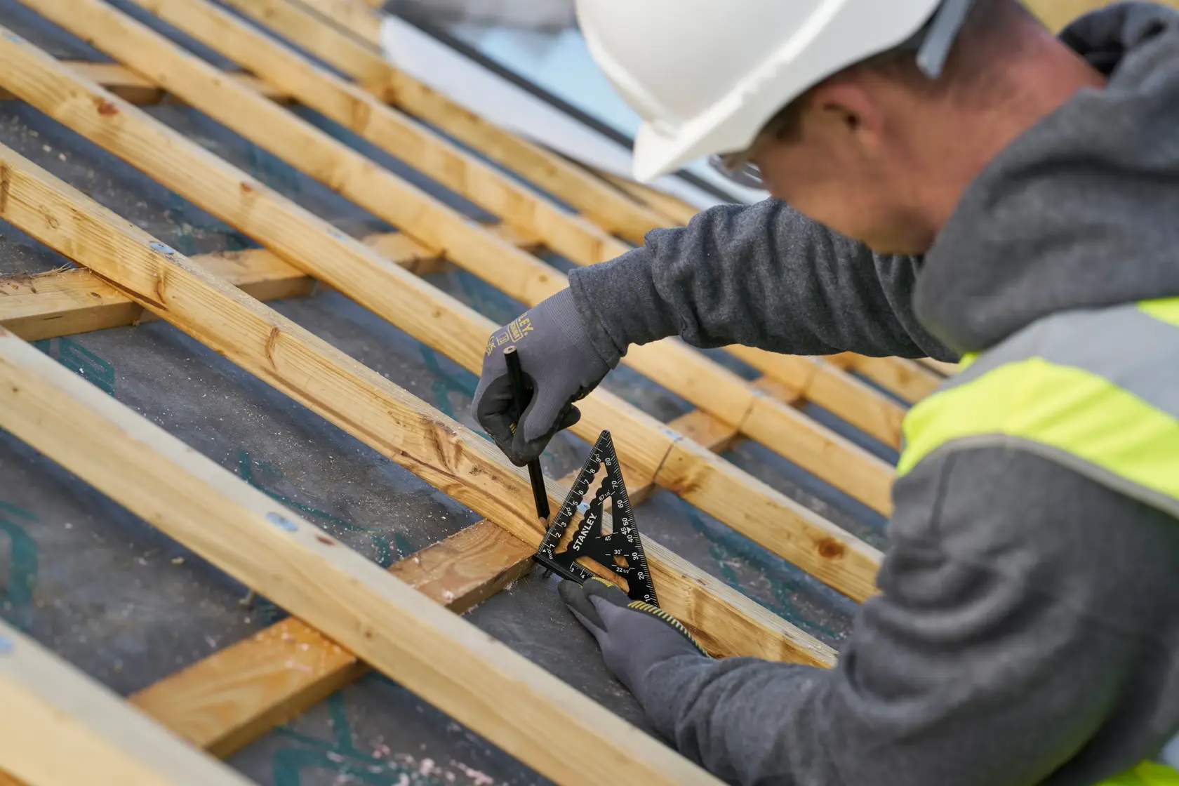 Foto della squadra nera STANLEY STHT46100-0 in uso su travi di legno, scena ravvicinata di cantiere.
