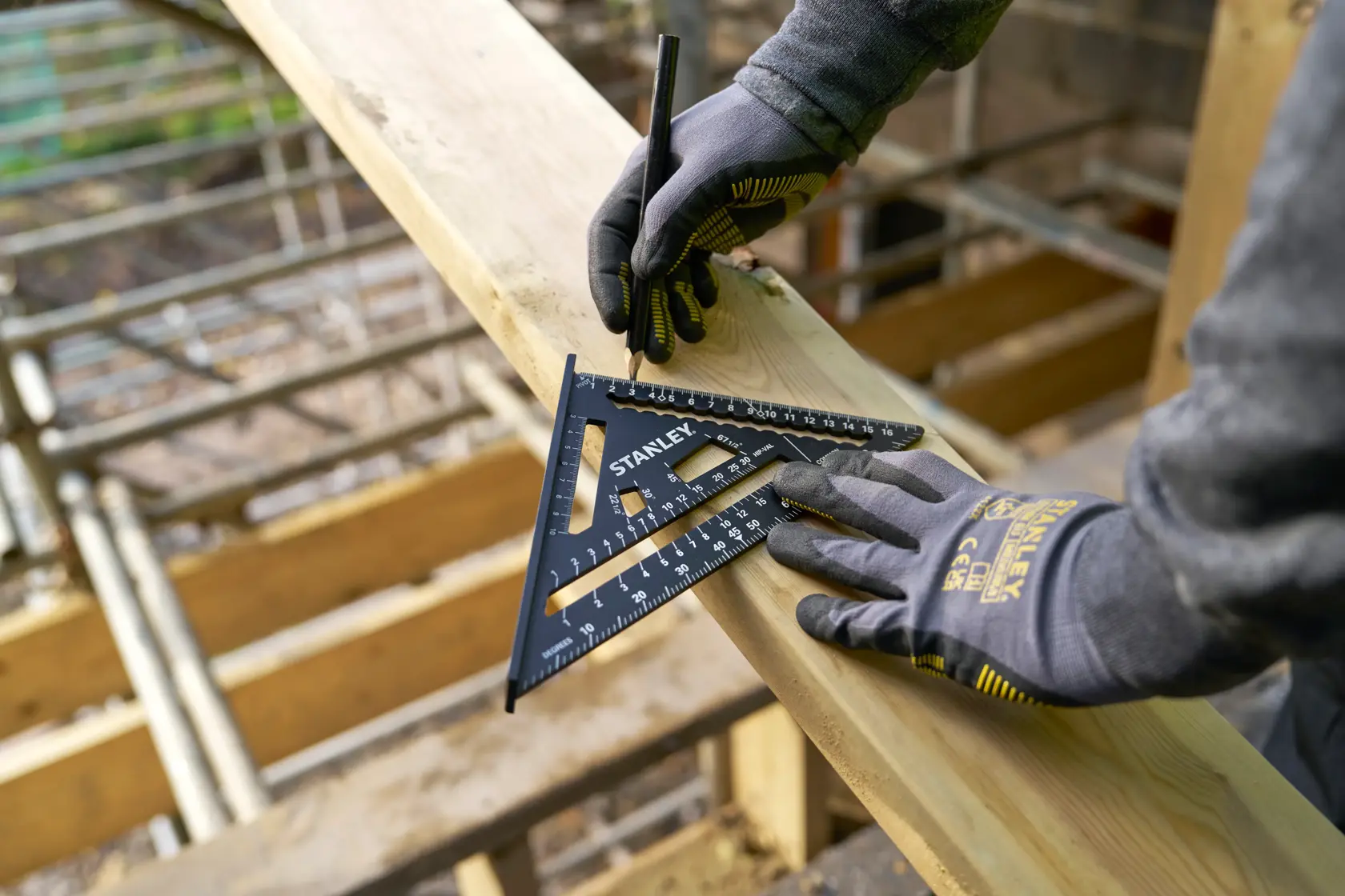 Squadra da carpentiere STANLEY STHT46101-0 per segnare il legno, mani con guanti, cantiere esterno.