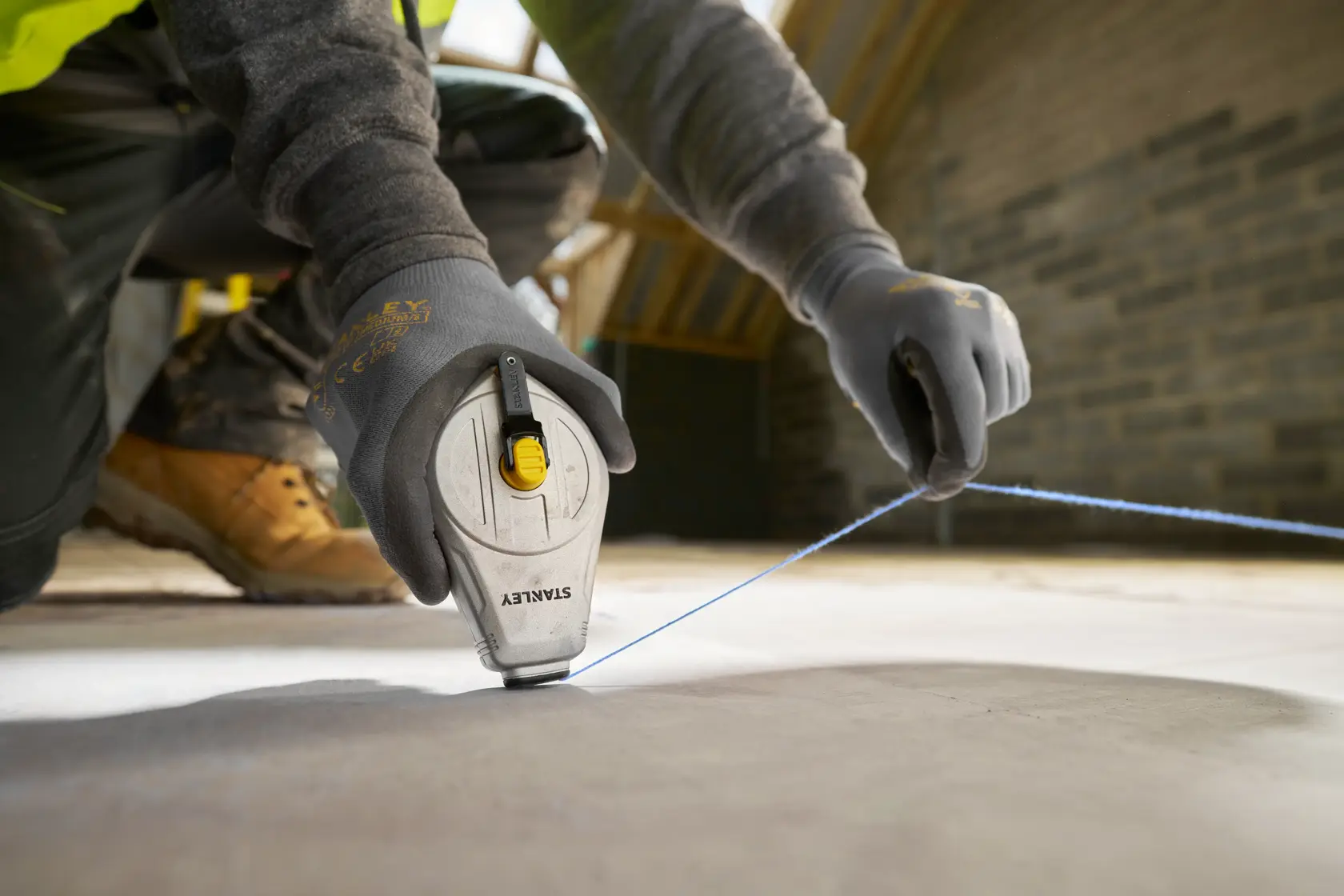 STANLEY STHT47110-0 traccialinee usato in cantiere, primo piano di mani con guanti che tirano il filo blu.