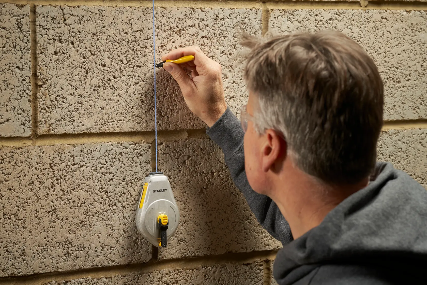 Rocchetto traccialinee STANLEY STHT47110-0 usato su muro di cemento con persona che traccia una linea retta.