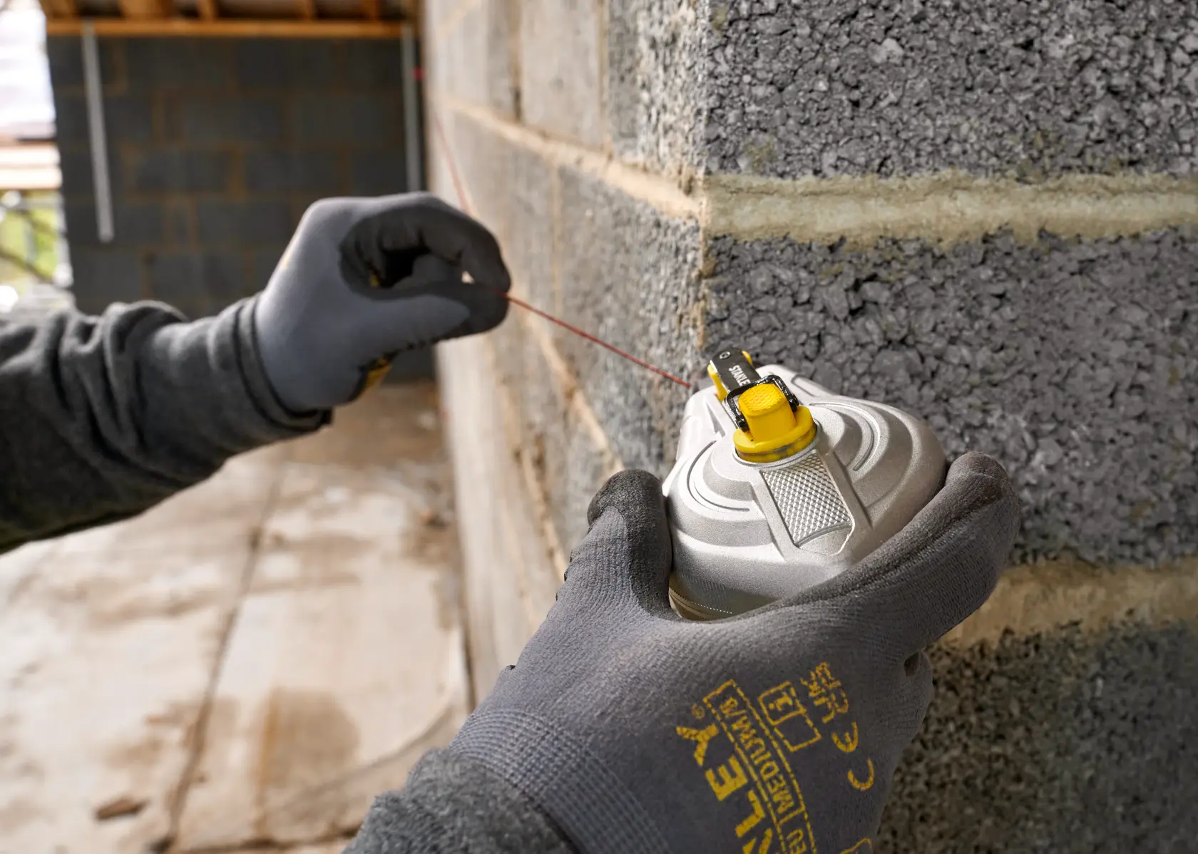 STANLEY STHT47611-0 strumento linea di gesso tenuto da mano guantata contro un muro di mattoni, fotografia ravvicinata.