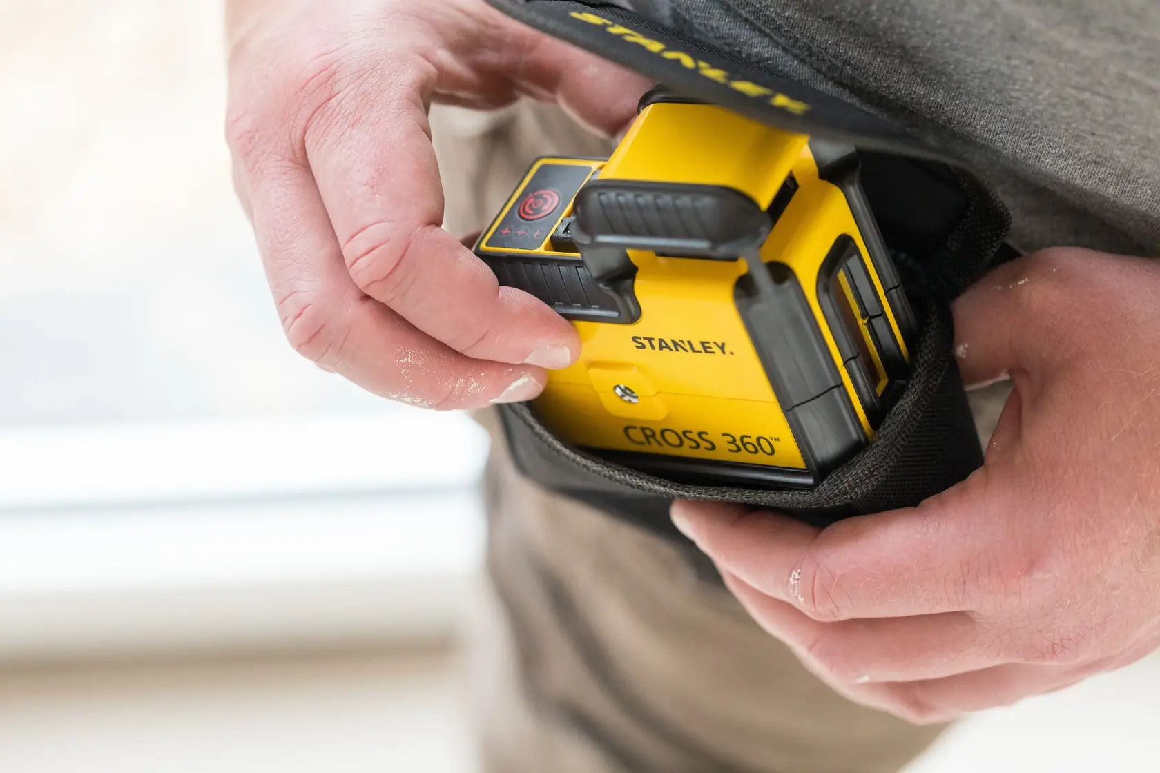 Gelber STANLEY STHT77504-1 CROSS 360° Linienlaser wird von Hand in eine schwarze Tasche gesteckt.