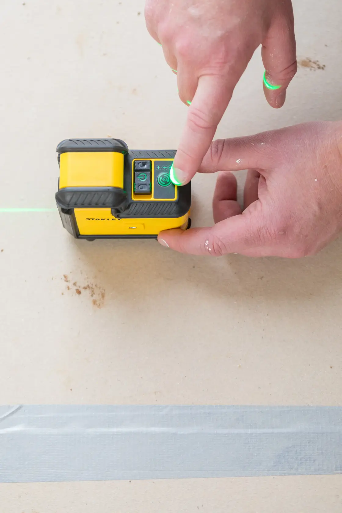 STANLEY STHT77594-1 Laser-Nivelliergerät in Betrieb, Nahaufnahme einer Hand, die den Netzschalter drückt, grüne Laserlinie sichtbar.