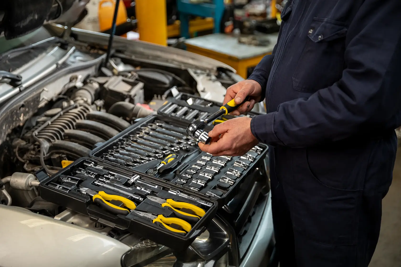 STANLEY STMT81243-LA tool set with yellow-handled pliers and sockets on car engine, mechanic using tools.