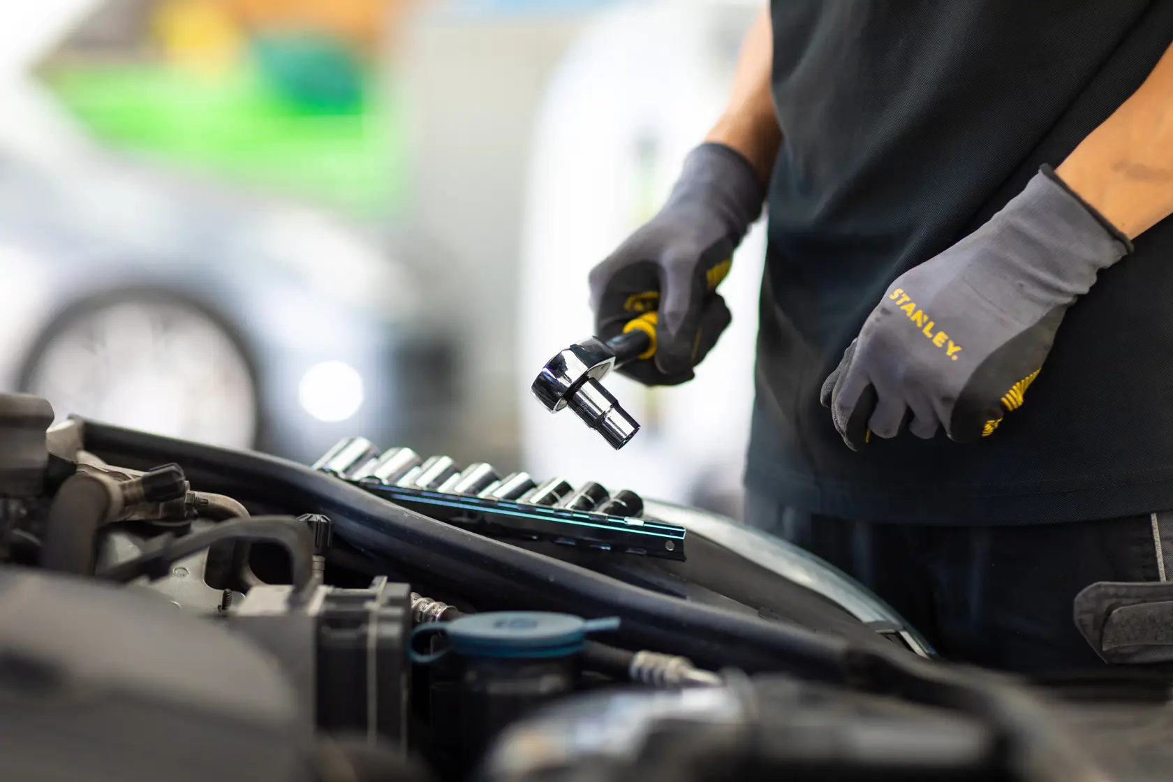 STANLEY STMT82671-0 ratchet and socket set in use, mechanic wearing STANLEY gloves near engine.