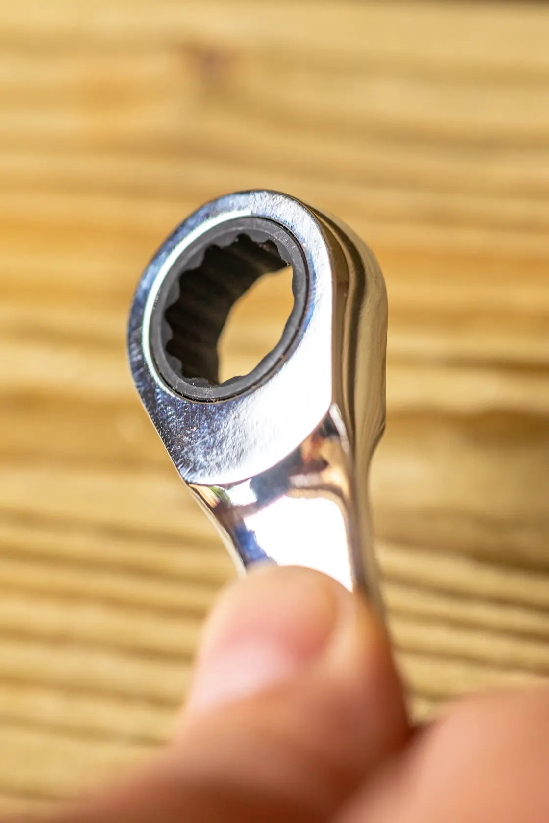 STANLEY STMT82846-0 close-up of chrome ratcheting wrench head, hand holding tool, wood background.