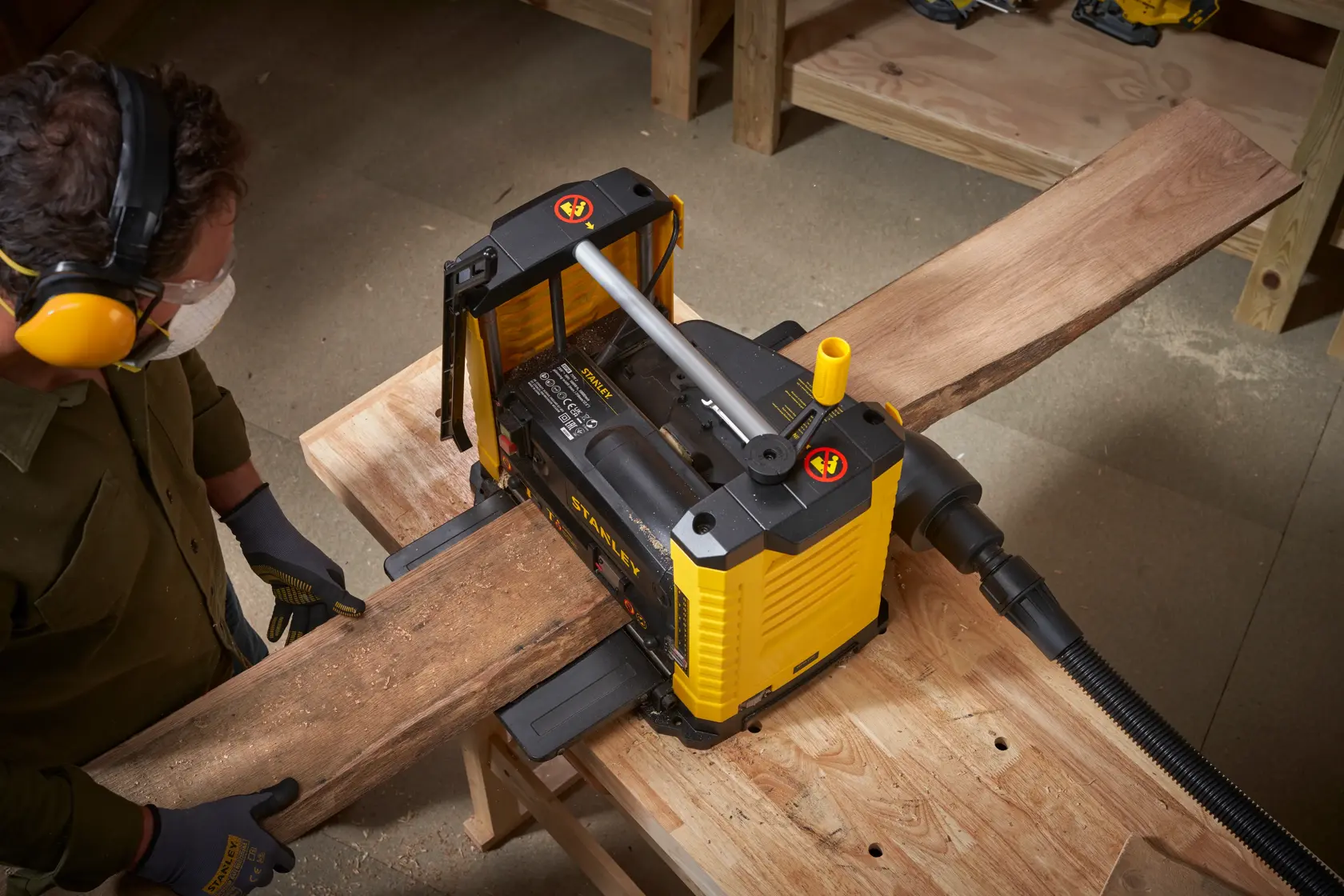 Photo de la raboteuse STANLEY STP18-B2 en utilisation, lissant une planche en bois dans un atelier vue du dessus.