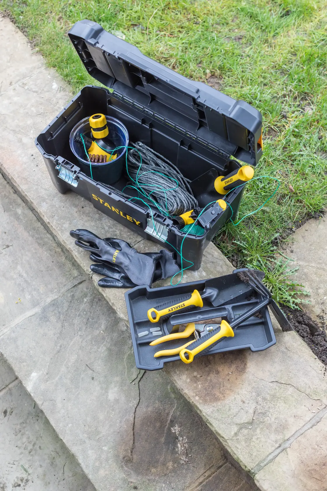 Stanley STST1-75521, STST1-75521-KR tool box with yellow-handled tools and gloves on outdoor stone.