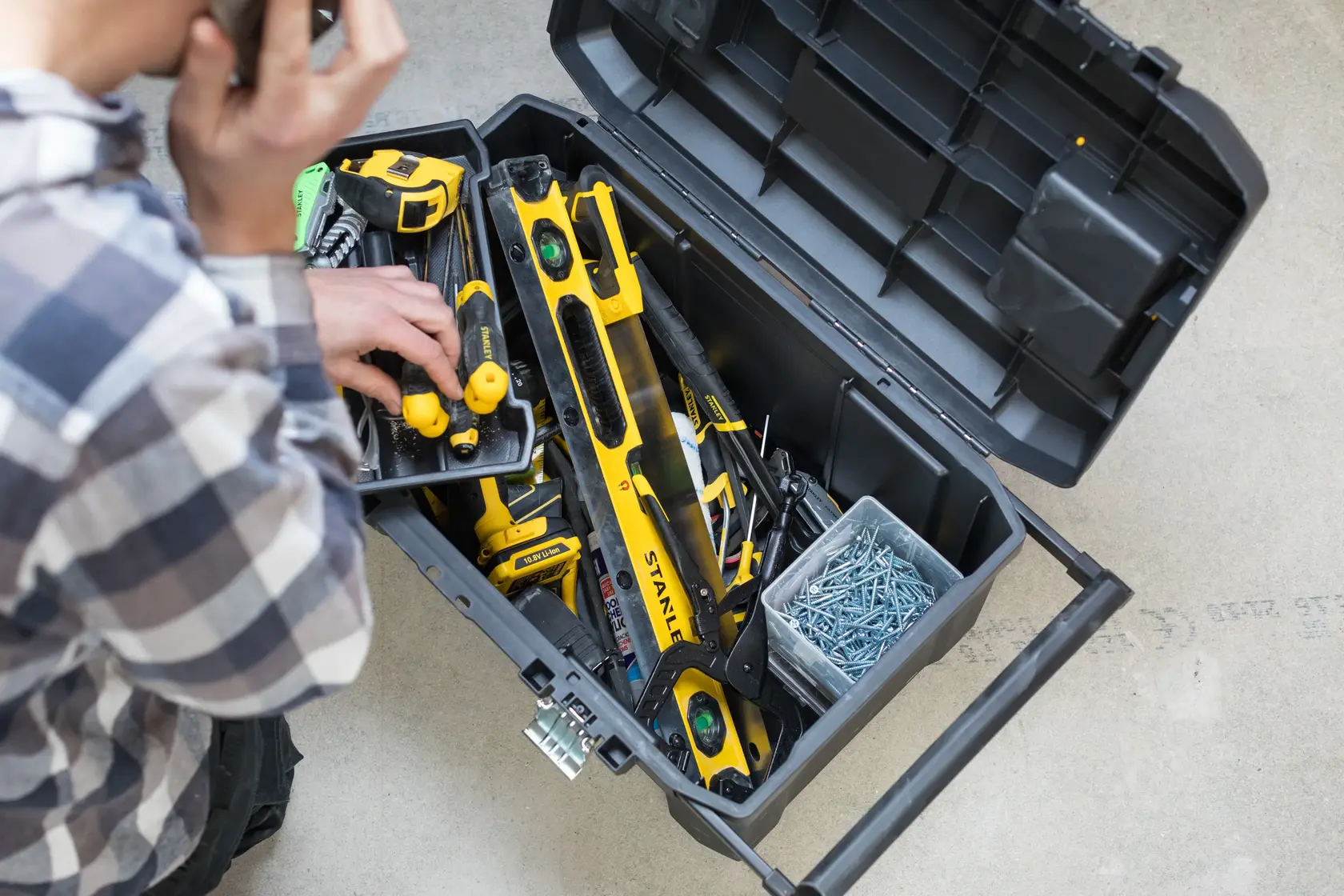 STANLEY STST1-80150 boîte à outils ouverte, vue de dessus avec outils jaunes et vis, main de l'utilisateur visible.