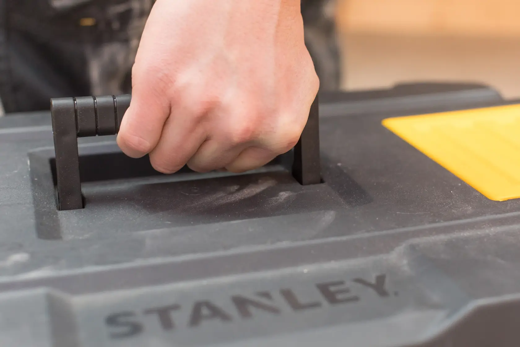 Poignée de boîte à outils STANLEY STST1-80150 en gros plan avec main, plastique noir et jaune.