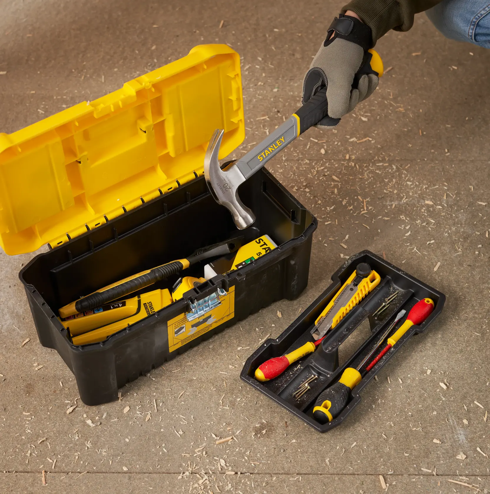 STANLEY STST75785-1 toolbox open on workshop floor with assorted hand tools and yellow removable tray.