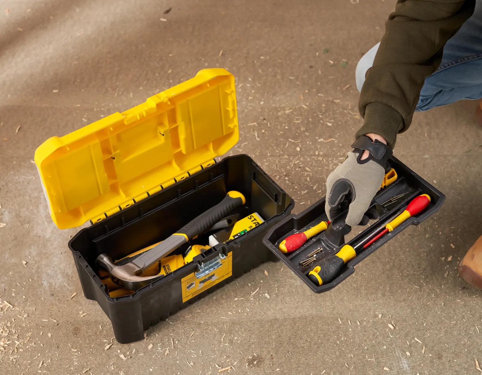 STANLEY STST75785-1 tool box with open lid, showing hand lifting tray with assorted hand tools on workshop floor.