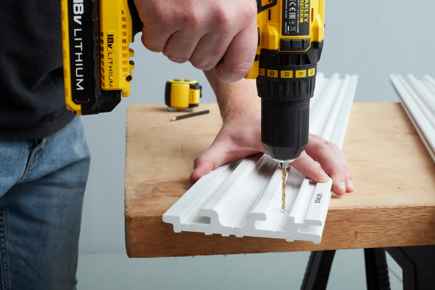 STANLEY STST82602-1 user drilling white plastic panel on workbench, close-up photography of product in use