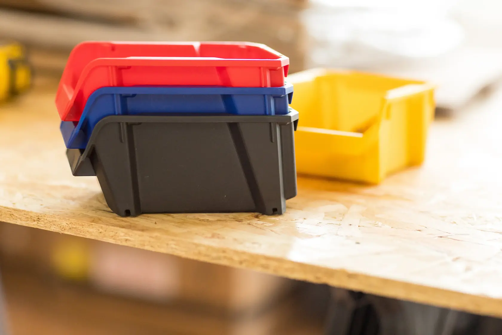 STANLEY STST82736-1 stapelbare Kunststoff-Aufbewahrungsboxen in Rot, Blau, Schwarz und Gelb auf Holzoberfläche.