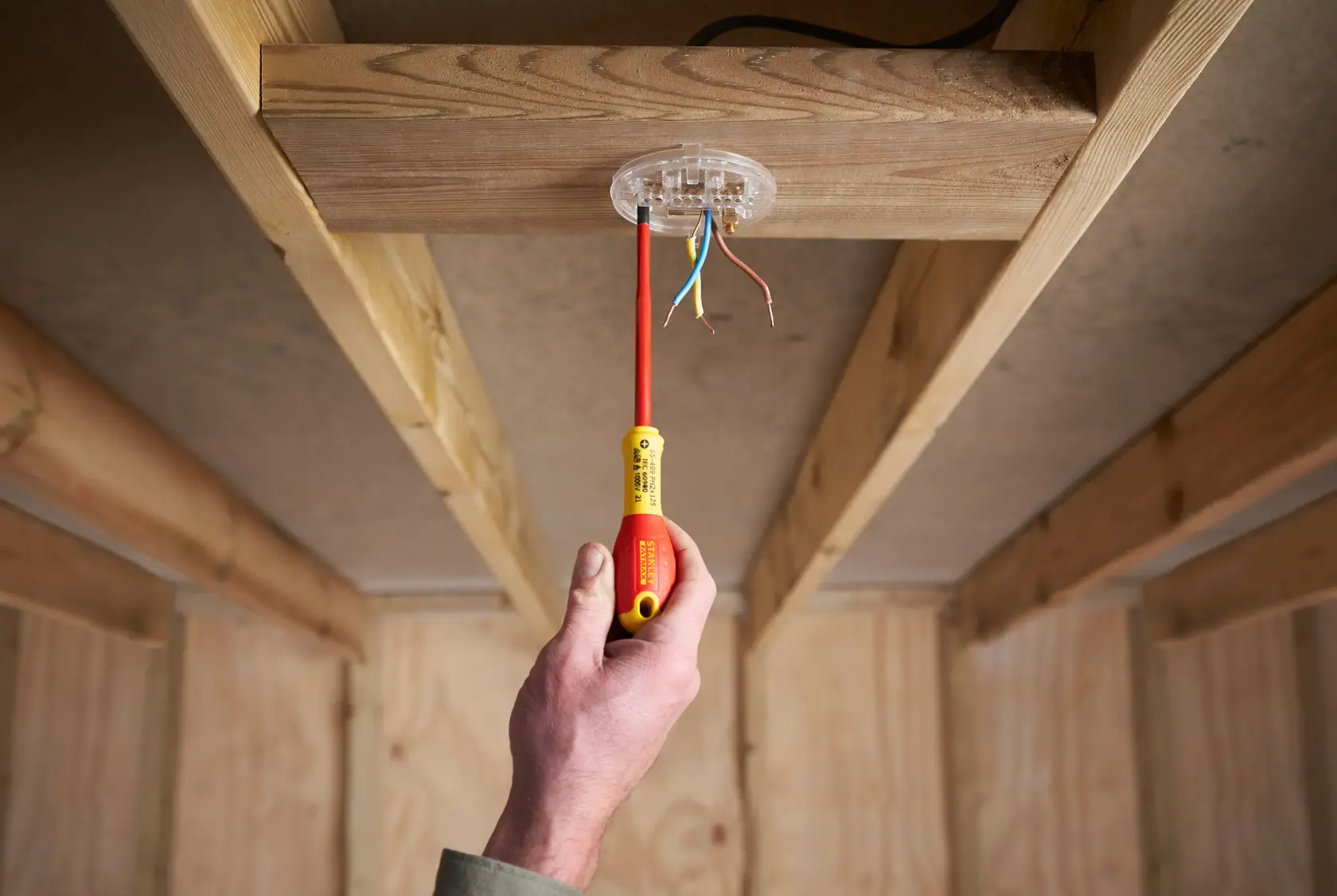 Photo of a hand using STANLEY XTHT0-62692 insulated screwdriver on ceiling wiring, indoor construction setting.