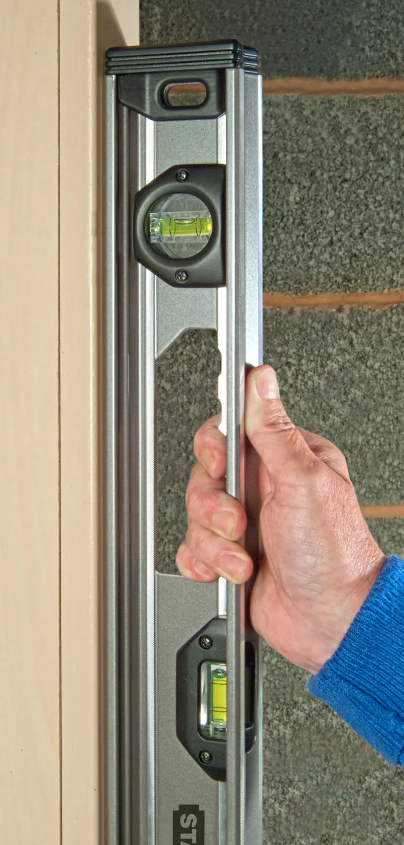 Niveau à bulle STANLEY XTHT1-42131 tenu verticalement par une main contre un cadre de porte.